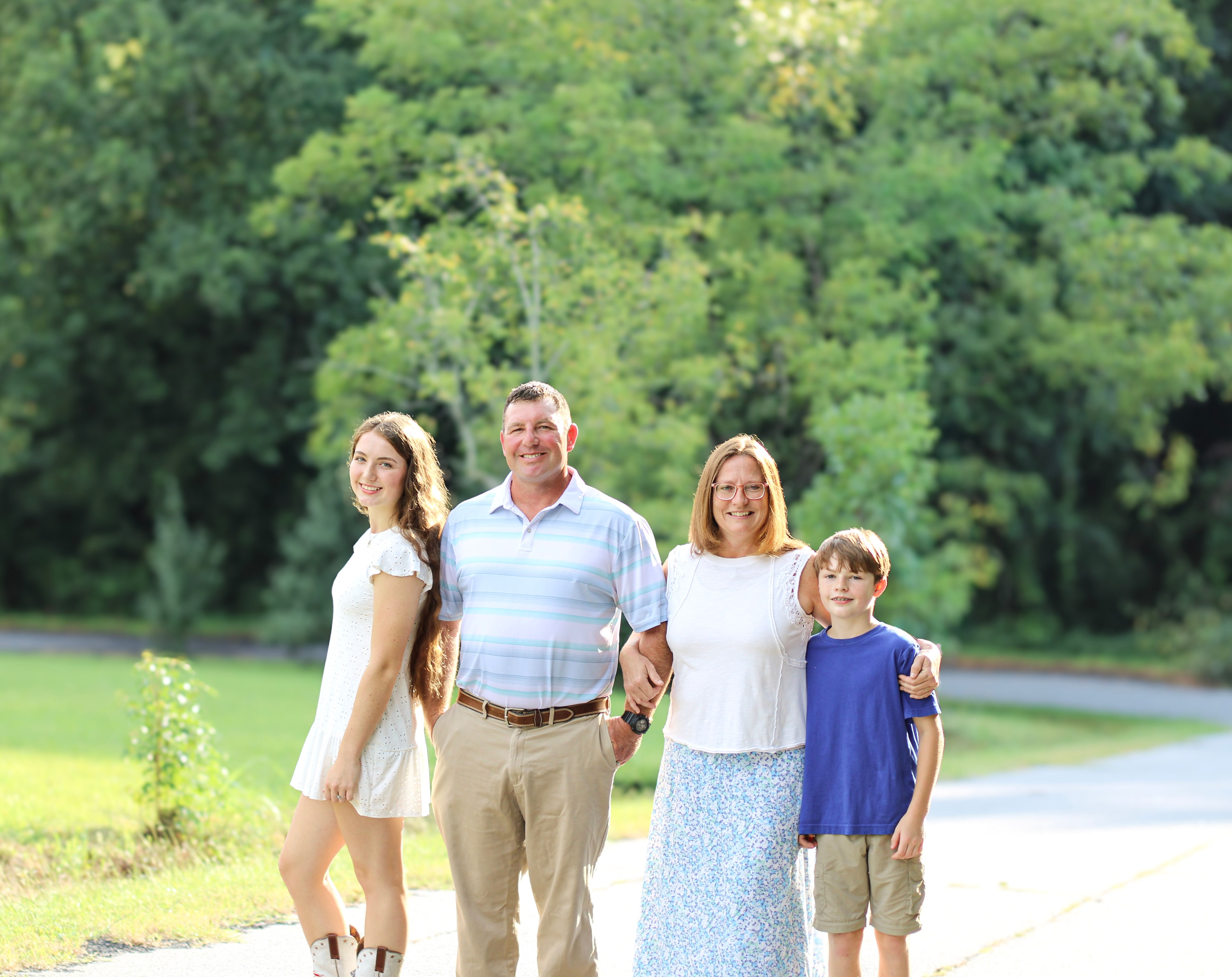 Family of four smiling outdoors on a park path