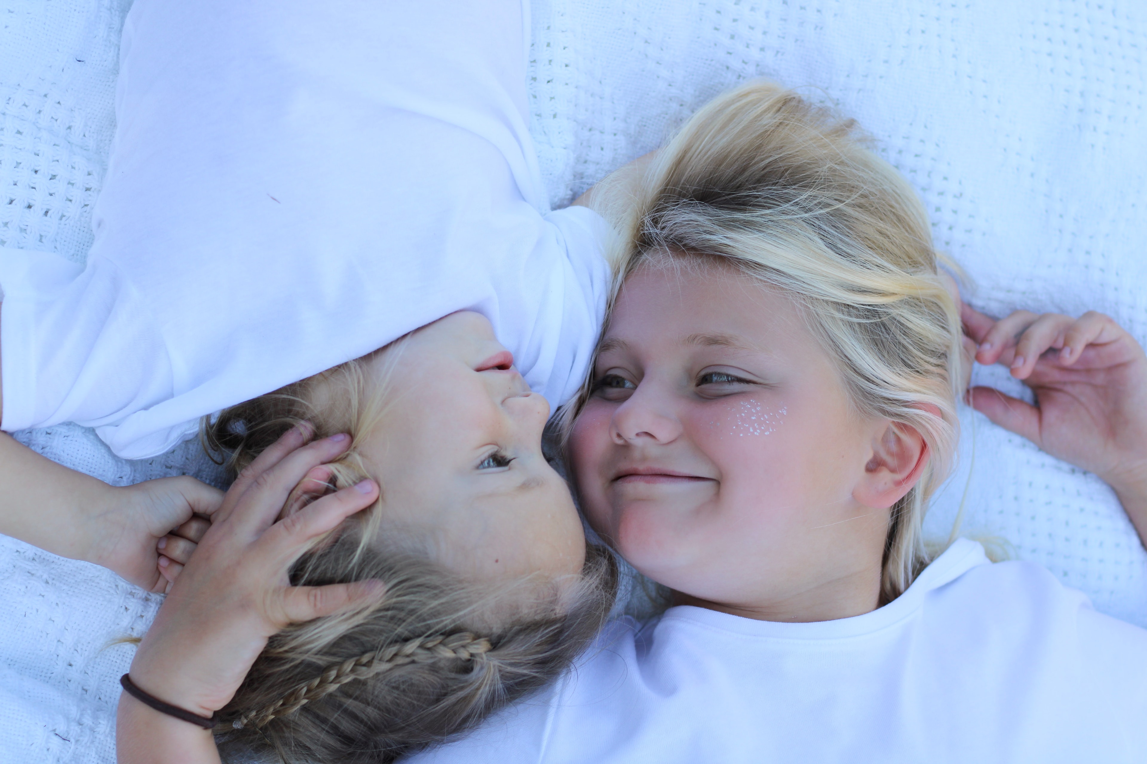 Two children lying on white bedding smiling